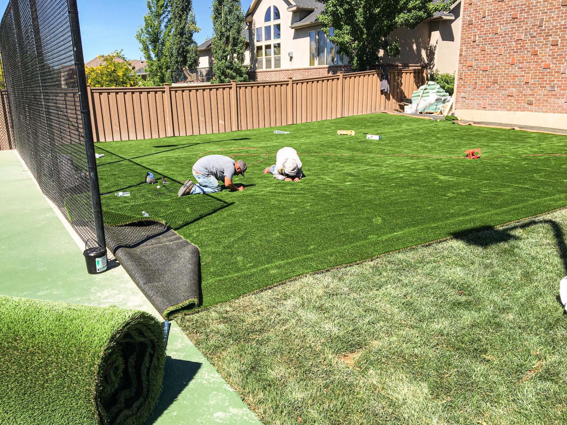 Simplified Landscaping crew installing synthetic turf in a backyard sport court area